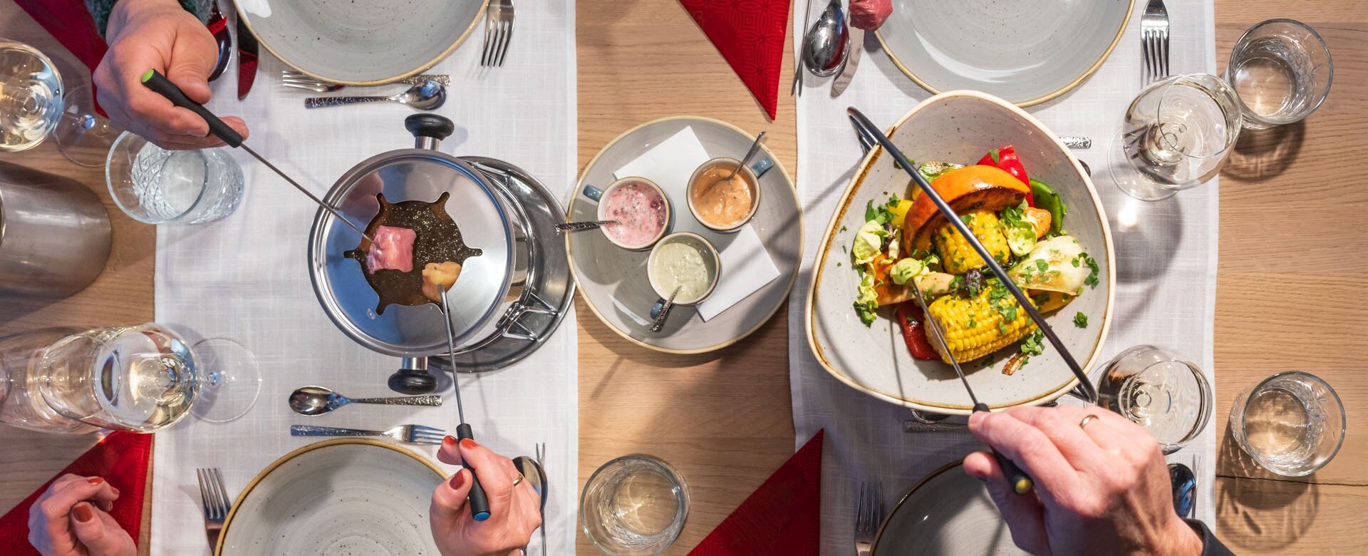 Vier Personen genießen Fleischfondue mit buntem Gemüse und Saucen an festlich gedecktem Tisch | © Martin Huber