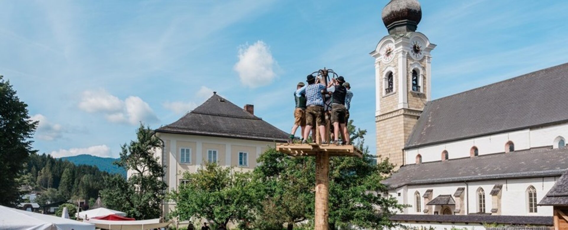Men in traditional dress stand on a climbing pole at a craft festival in Altenmarkt, audience watches from benches outside. | © Matthias Fritzenwallner