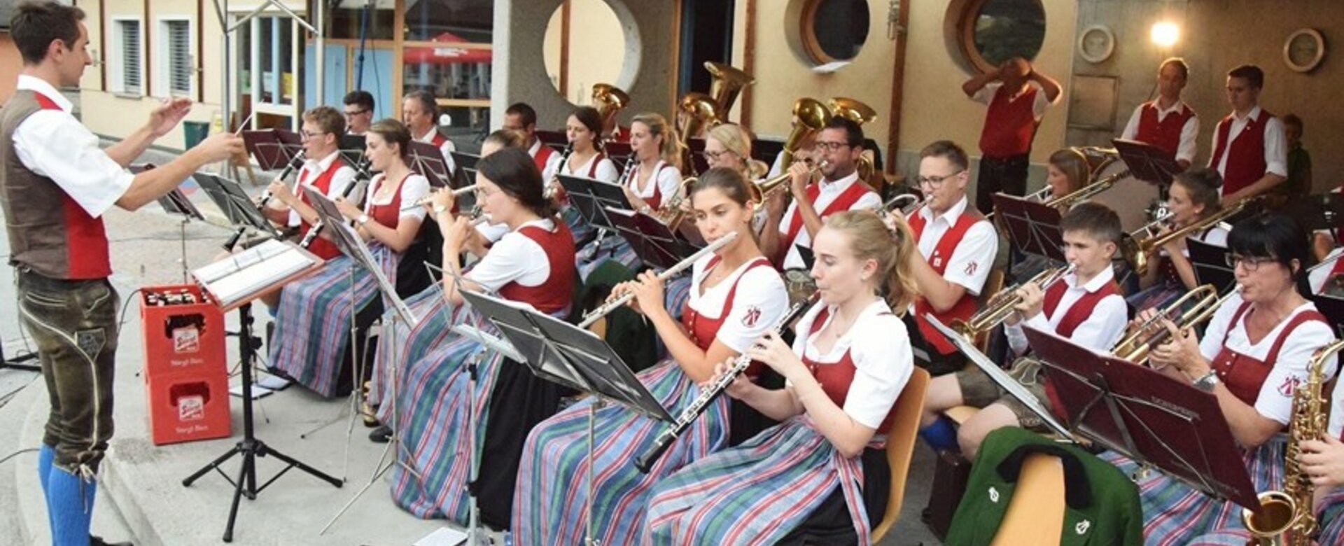 Brass band in traditional dress performs at village evening near round-window building