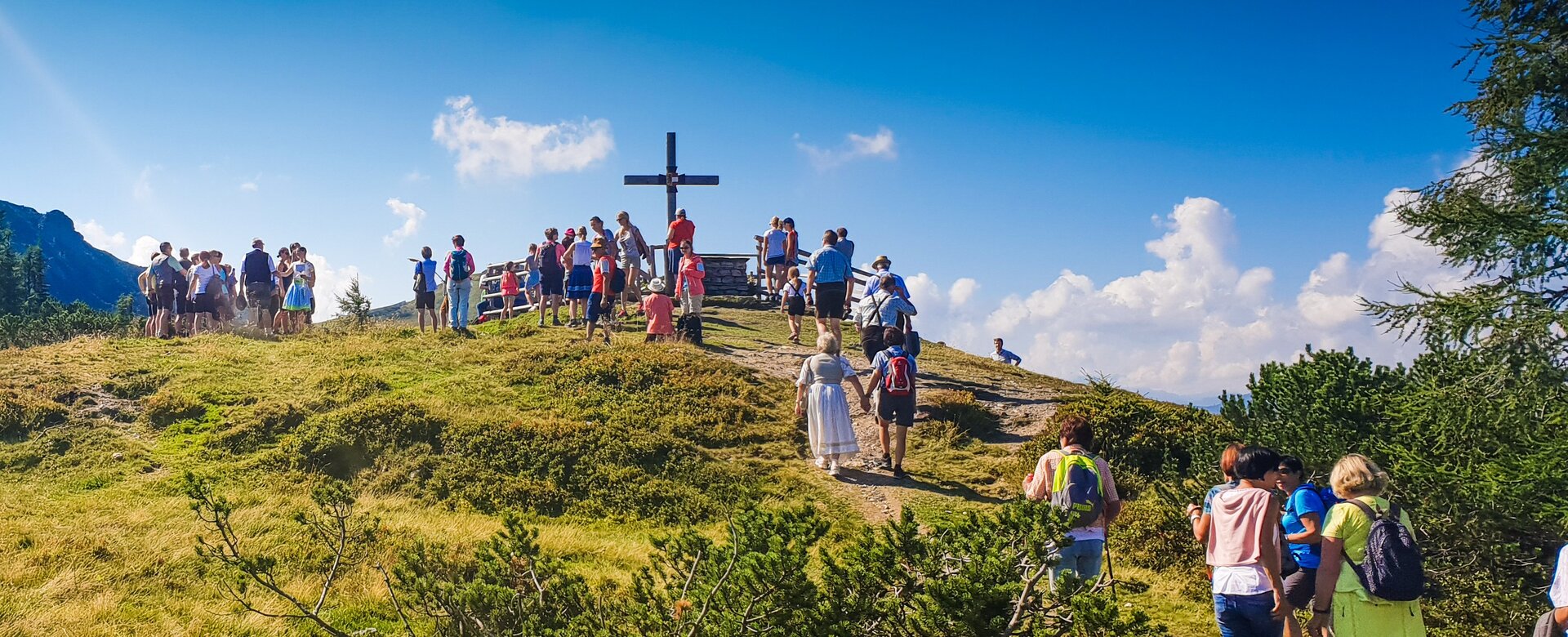 Gruppe von Menschen wandert bei Sonnenschein zur Bergmesse am Gipfelkreuz in Flachau | © Flachau Tourismus