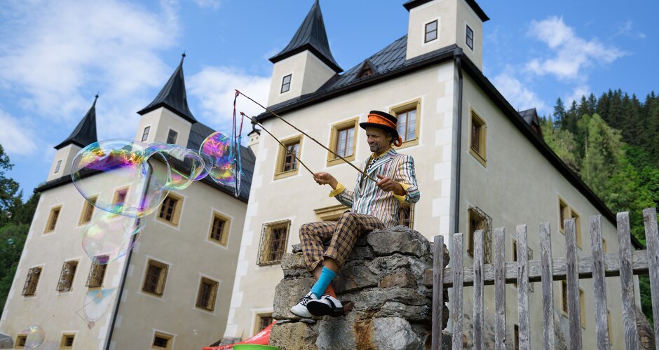 Performer in colorful outfit creates giant soap bubbles in front of Schloss Höch | © Flachau Tourismus
