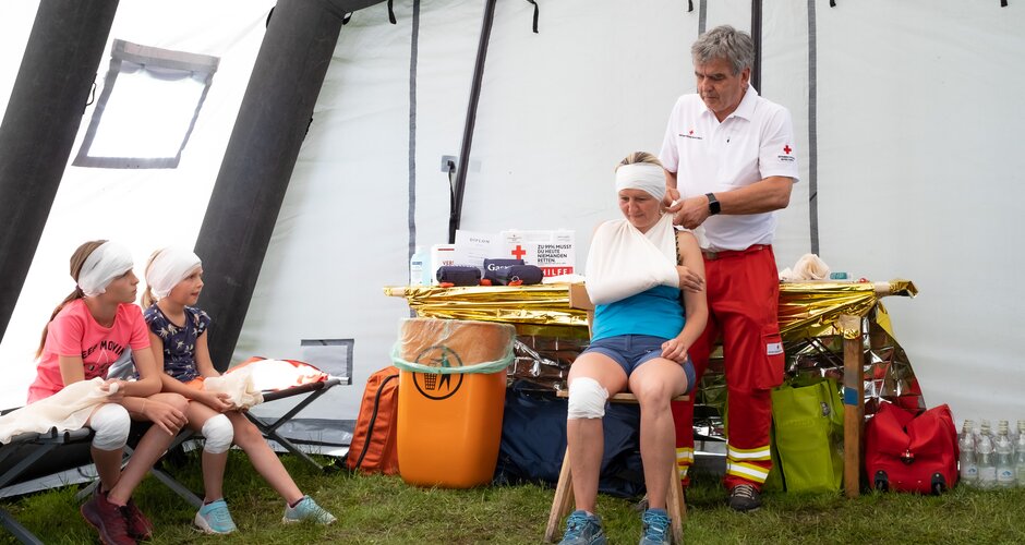 Ein Sanitäter legt einer Frau mit Verband am Kopf eine Schulterschlinge an