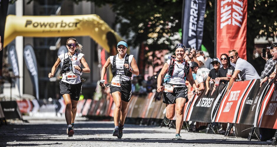 Three female trail runners finishing the adidas INFINITE TRAILS, smiling with cheering spectators in the background | © Gasteinertal Tourismus GmbH, Sportograf