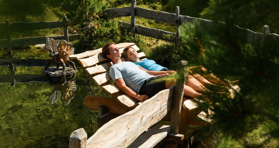 Ein Paar liegt auf einer großen Holzliege inmitten der Natur und sonnt sich | © marktl photography für Gasteiner Bergbahnen AG