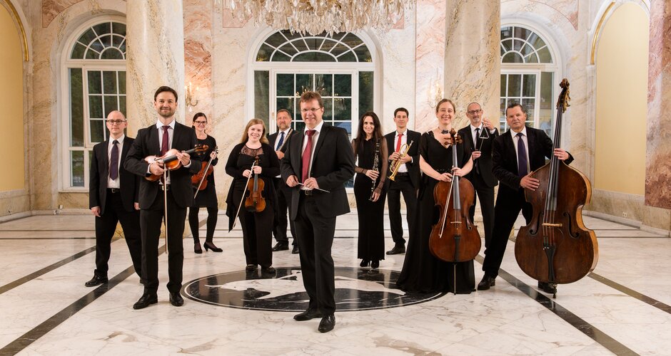 Bad Gastein spa orchestra with instruments in a marble hall, formally dressed in front of an ornate chandelier | © KTVB Bad Gastein, Marktl Photography