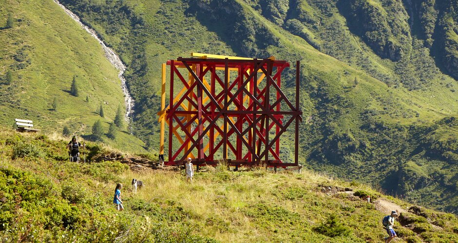 Large wooden structure in red-orange tones stands in the middle of the mountain | © Florian Kolmer