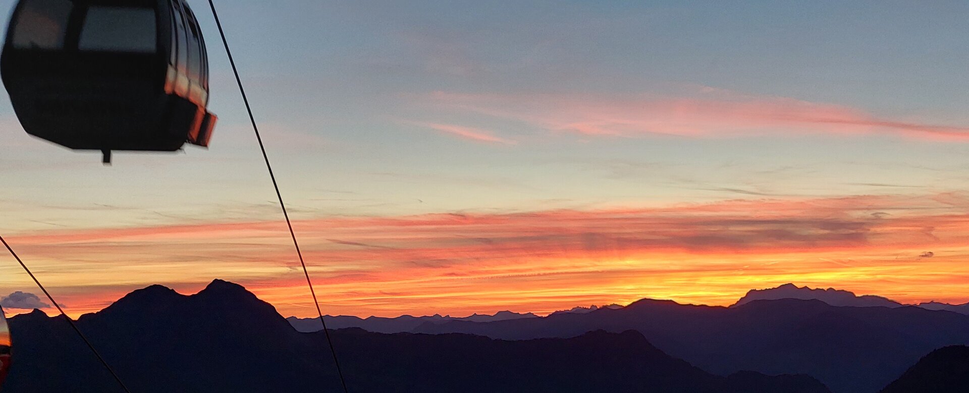 Gondola floats at sunset above mountain landscape with colorful evening sky and silhouettes