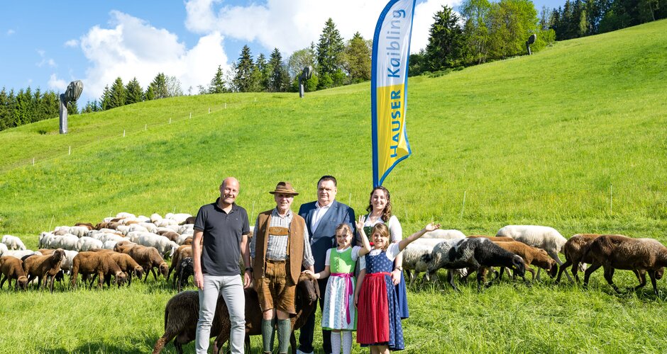 Four adults and three children stand in front of a flock of sheep and a Hauser Kaibling flag flies in the background | © Hauser Kaibling