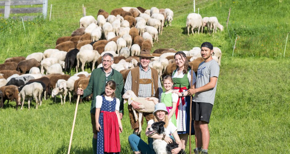 Two shepherds and other people standing in front of a flock of sheep with a dog and a lamb | © Hauser Kaibling