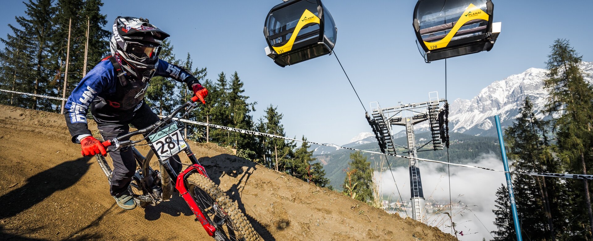 Mountain biker with race number rides downhill under gondolas at Planai on dirt trail | © Vladimir Stanescu