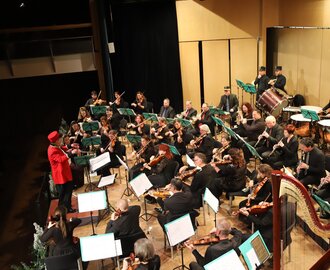 Large orchestra with conductor in red coat at Sinfonietta St. Johann concert, many strings and wind instruments | © Jocongress
