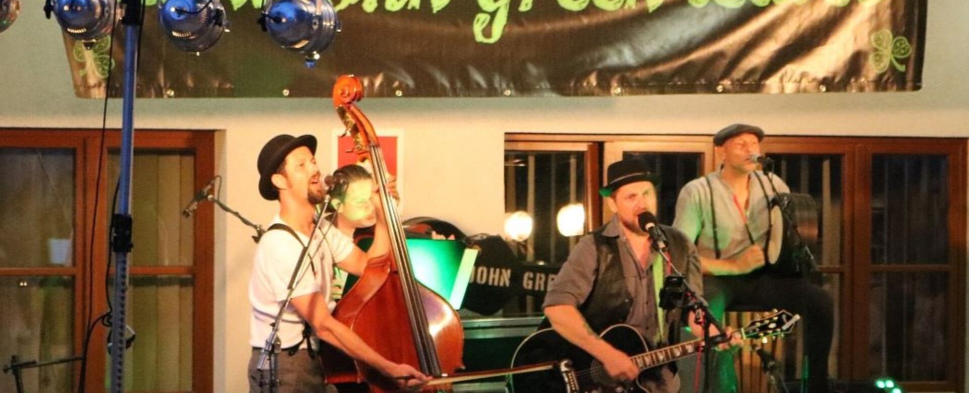 Three musicians on stage with double bass, guitar and drum, banner says “John Green Leaves” | © Wagrain-Kleinarl Tourismus