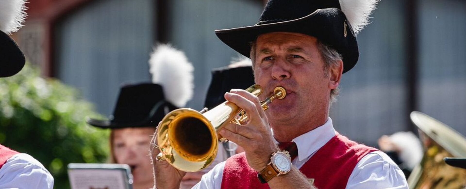Mann in Tracht mit Federhut spielt Trompete, weitere Musiker im Hintergrund sichtbar | © Wagrain-Kleinarl Tourismus