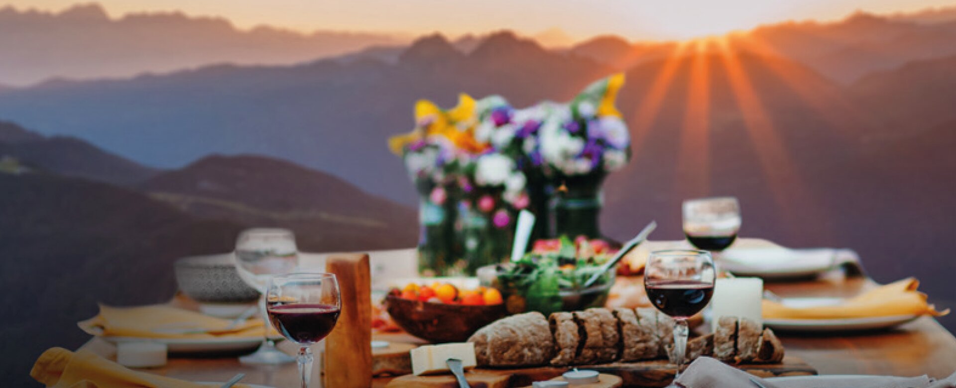 Wooden table with wine, bread, cheese and flowers at mountain dinner during sunset