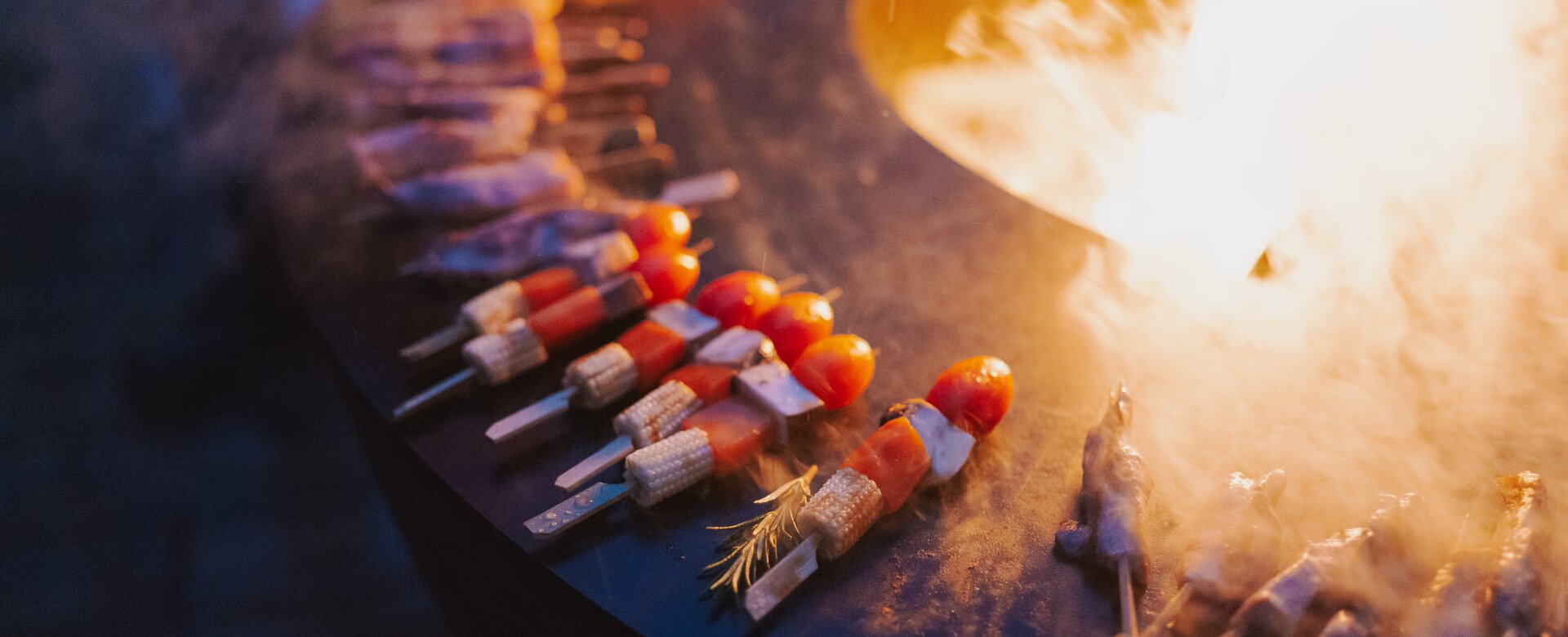 Skewers lie on a metal surface and an open fire can be seen in the centre | © Christian Schartner