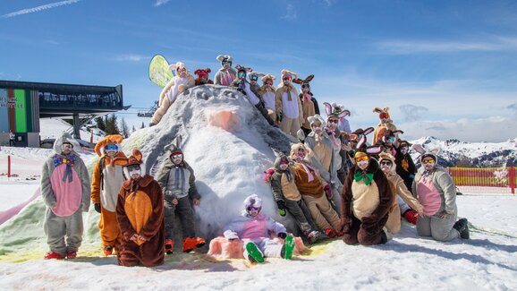 Gruppe verkleideter Skifahrer als Osterhasen posiert auf Schneehügel bei Sonnenschein im Skigebiet | © Shuttleberg