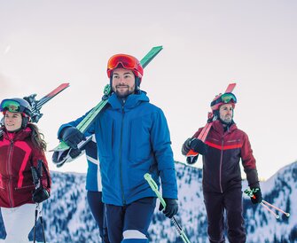 Four skiers carrying their skis on their shoulders – the perfect start for the Back2Ski course, a program for returning skiers. | © Ski amadé