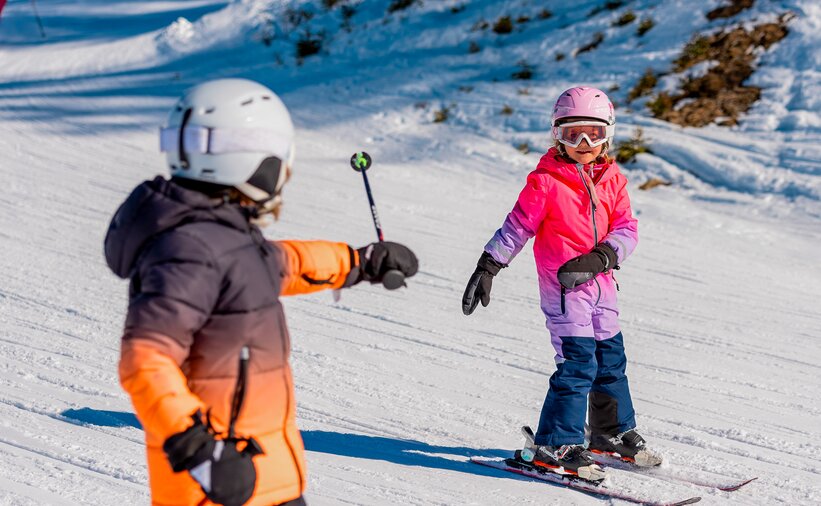 Two children in a ski course on a slope, one pointing at the other with a ski pole. | © Hochkönig Tourismus GmbH