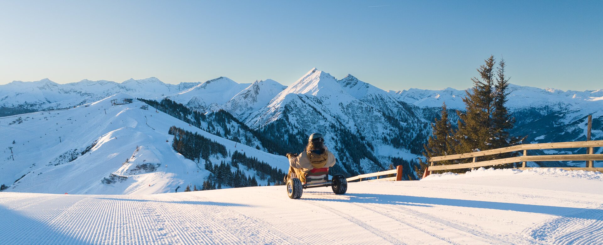 Person rides snow kart on freshly groomed slope with view of snowy mountains in bright sunshine. | © Dorfgasteiner Bergbahnen AG