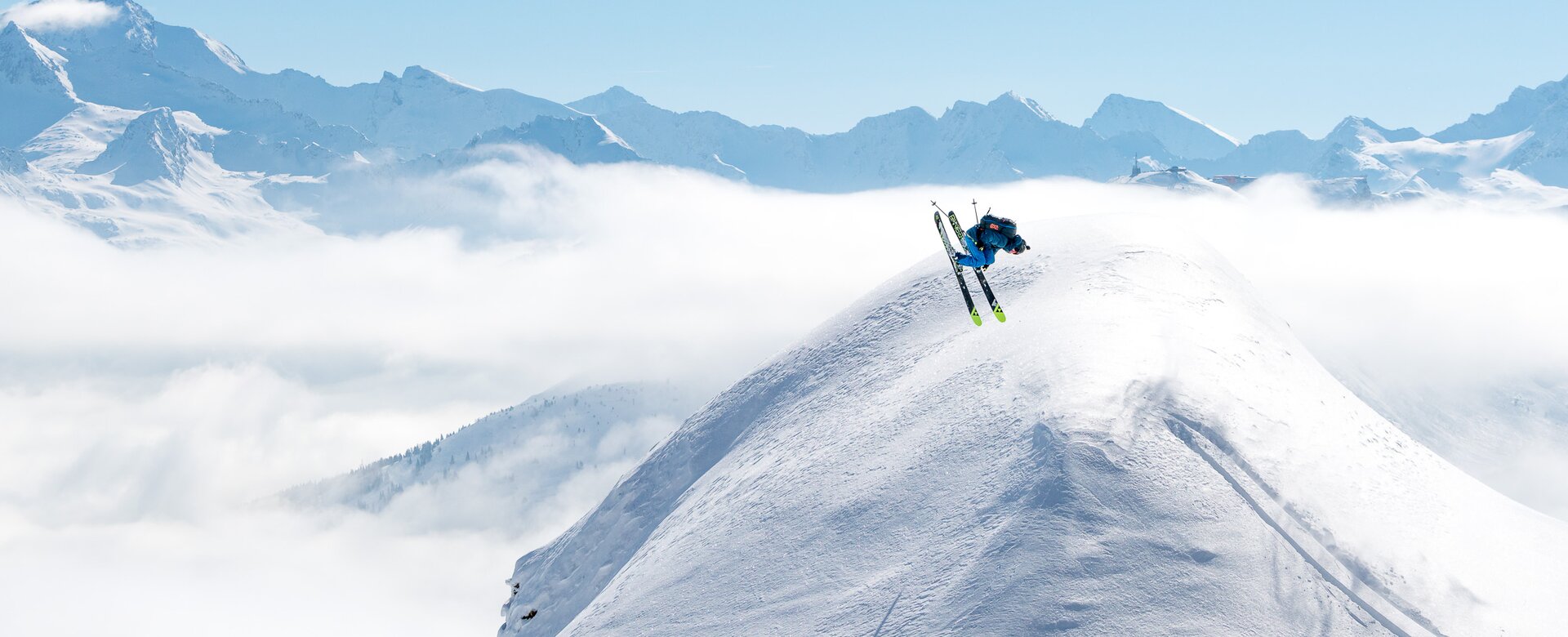 Skifahrer mach einen Backflip über eine Schneekuppel und rundherum sind verschneite Berge und ein blauer Himmel zu sehen | © Gasteinertal Tourismus GmbH, www.oberschneider