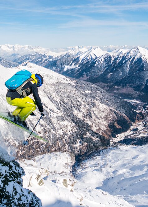 Skifahrer mit Rucksack springt über eine Klippe und man sieht in das von Bergen gesäumte Gasteinertal | © www.oberschneider