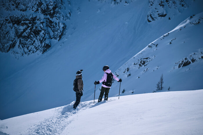 Zwei Freerider mit Helmen stehen im Tiefschnee vor steilem Hang und besprechen ihre Abfahrtsroute | © Liftgesellschaft Zauchensee/C.Schartner