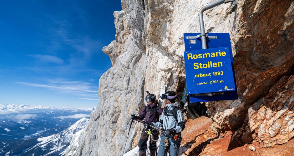 Two freeriders stand at Rosmarie Tunnel on a snowy, steep rocky mountain face | © Josh Absenger