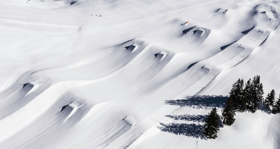 Aerial view of Kings Park Hochkönig showing fresh powder, shaped jumps, rails and distinct tree shadows on the snow.