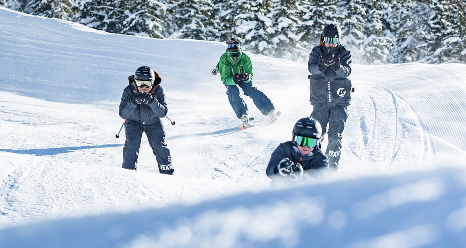 Five youths with helmets and skis riding dynamically on snowy track at Shuttleberg ski resort | © Shuttleberg