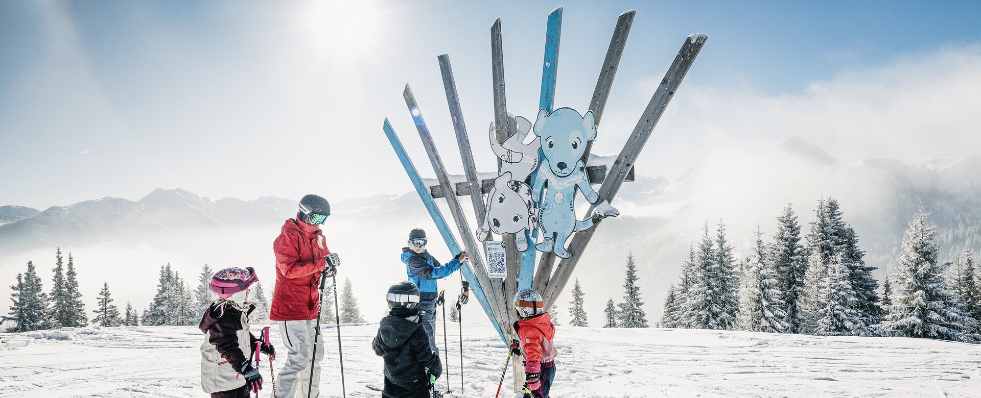 Kids with adult on skis in front of wooden sculpture with animals on Family Run at Shuttleberg resort | © Shuttleberg