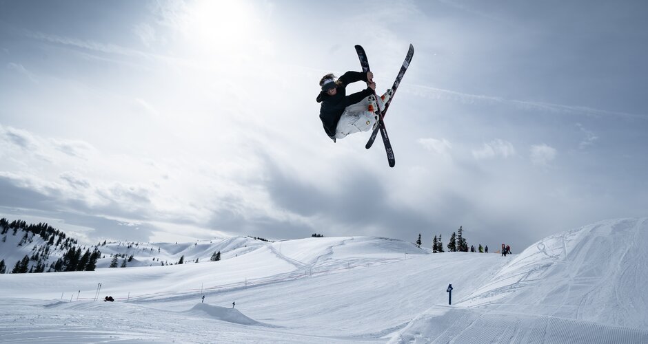 A freestyler jumps over a jump in Kings Park and does a trick with crossed skis.