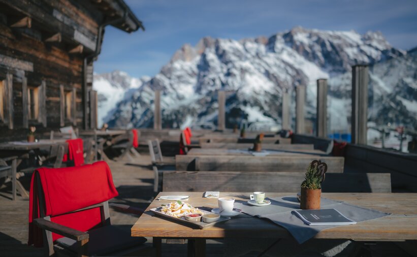 Servierter Kaiserschmarrn mit Puderzucker und Kaffee auf Holztisch, leere Terrasse vor Alpenpanorama | © Ski amadé