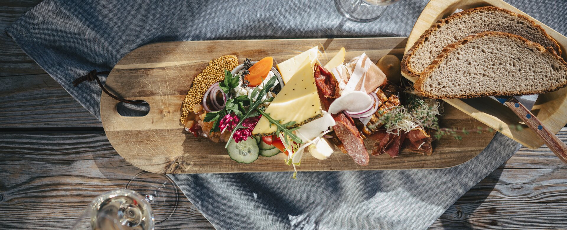 Cheese, cold cuts, bread, vegetables and herbs arranged on wooden board with two glasses of white wine | © Ski amadé