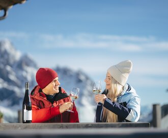 Man and woman toast with white wine, snowy mountains and church tower visible in background | © Ski amadé