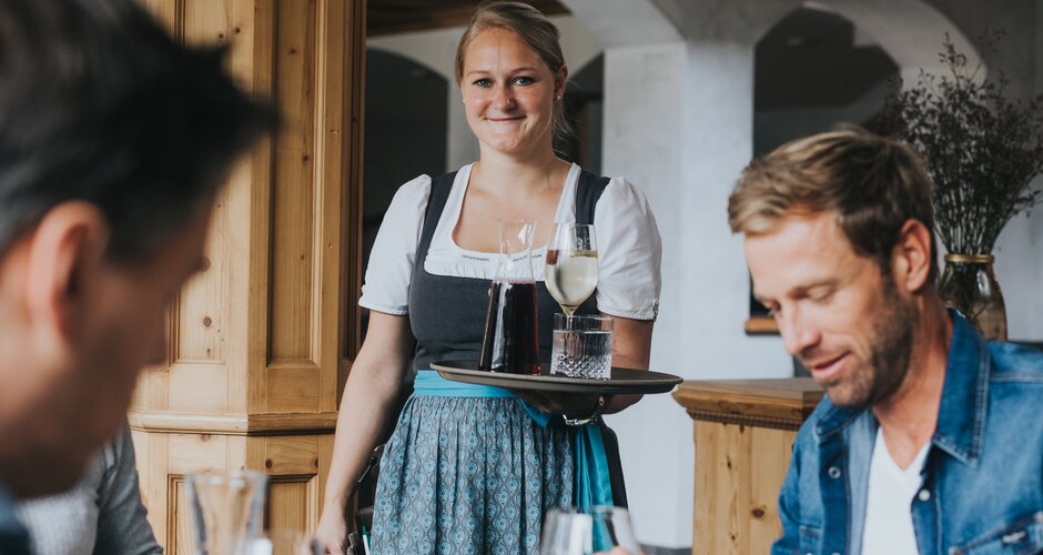 Waitress in dirndl serving red and white wine at the hotel restaurant