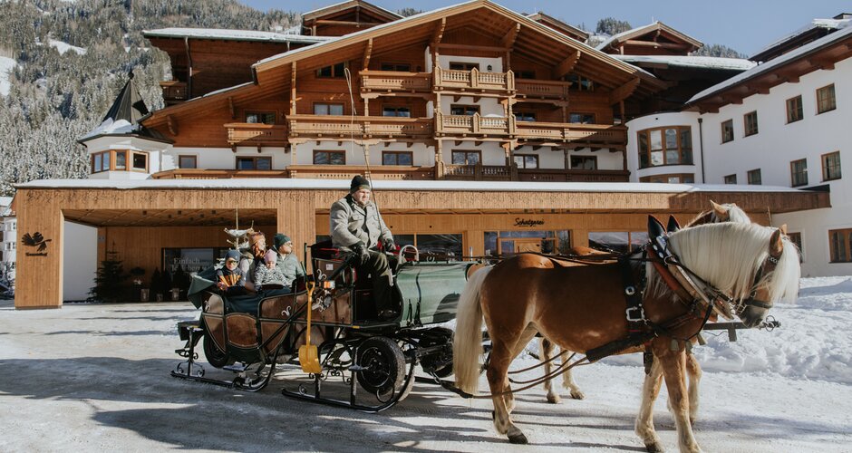 Horse sleigh with driver and guests in front of snowy Hotel Tauernhof