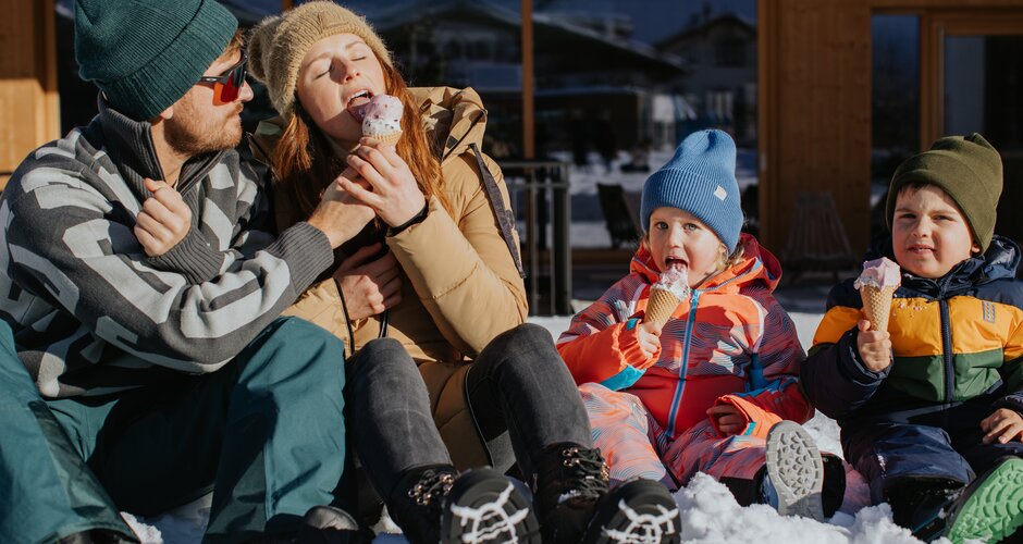 Two adults and two children eating ice cream in snow wearing winter clothes