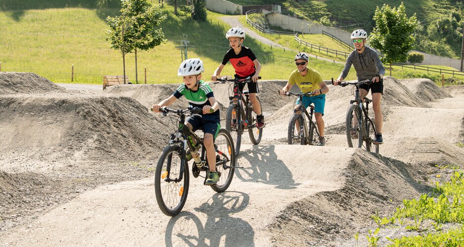 Two kids and two adults ride with helmets over waves and curves at Pumptrack Dorfgastein | © Gasteinertal Tourismus GmbH, Fotoatelier Wolkersdorfer