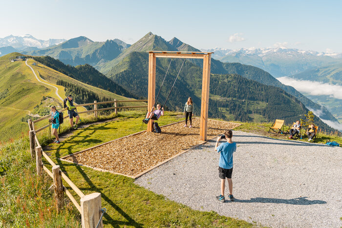 Jugendliche schaukeln vor Bergpanorama, andere machen Pause oder fotografieren am Gipfel | © Dorfgasteiner Bergbahnen AG