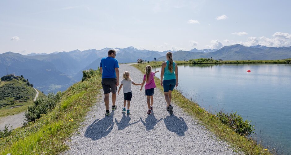 Familie wandert bei Sonnenschein am Bergsee entlang mit Blick auf die Gasteiner Alpen | © Gasteiner Bergbahnen AG