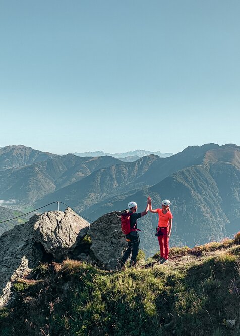 Zwei Kletterer geben sich ein High-Five am gesicherten Klettersteig mit weitem Blick über das Gasteinertal | © Gasteiner Bergbahnen AG