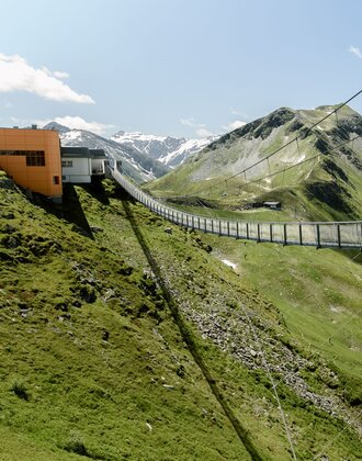 Long suspension bridge at Stubnerkogel leads from top station over slope with view of snow-capped peaks | © Gasteiner Bergbahnen, Marktl Photography