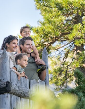 Family with two kids on wooden platform in Graukogel pine forest, looking into the distance | © Skigastein, seven frames