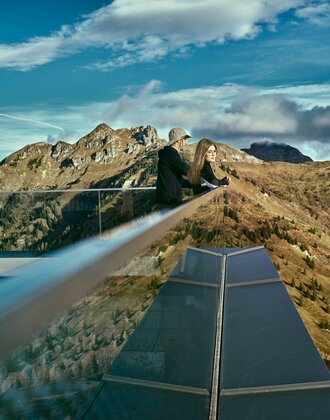 Two people enjoying the alpine view from the modern lookout at Kieserl in Großarl, surrounded by autumn-colored mountains. | © Großarler Bergbahnen