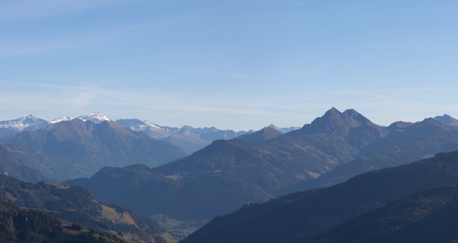 Panoramablick von Maria Alm auf bewaldete Hügel und schneebedeckte Gipfel im Salzburger Land im klaren Herbstlicht