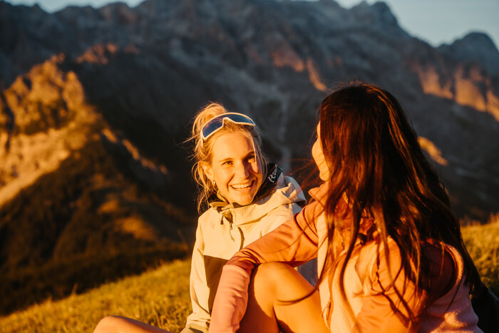 Two female hikers sit in evening light in Dienten with a rocky mountain massif near Gabühelbahn. | © Hochkönig Bergbahnen