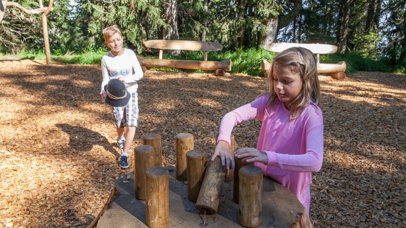 Zwei Kinder spielen mit Holzklötzen an Mitmachstation im Almspielplatz Hochkönig, umgeben von Wald und Natur