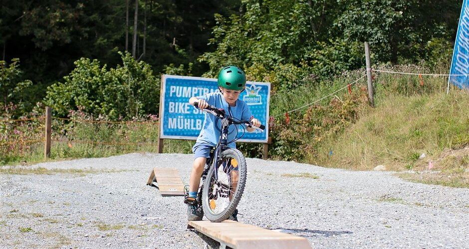 Child with green helmet balancing on wooden ramp at Pumptrack & Skill Area Mühlbach