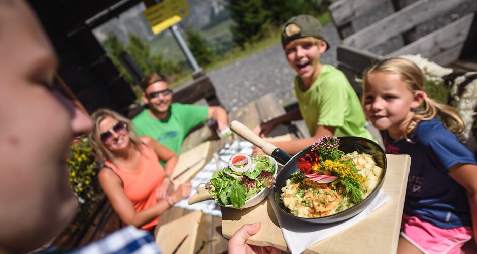 Eine Servicekraft bringt einer Familie auf der Sonnenterrasse der Karbachalm in Mühlbach ein Gericht mit Salat. | © Hochkönig Bergbahnen
