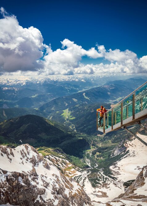 Zwei Personen stehen auf der gläsernen Treppe ins Nichts am Dachstein über einer tiefen, grünen Gebirgslandschaft. | © Christoph Huber